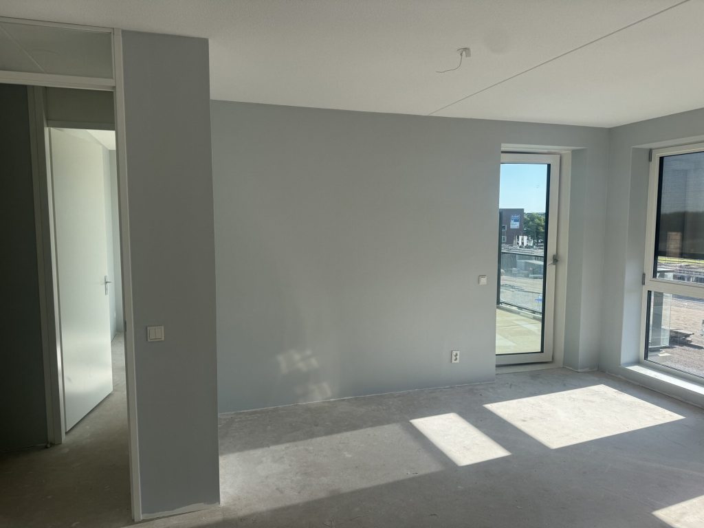Lege woonkamer in een nieuw appartement met lichte wanden, een balkondeur en een betonvloer