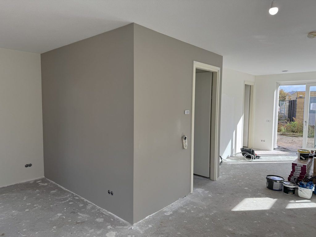 Pas afgewerkte grijze wand in een nieuwe woning, met verfemmers op de betonvloer